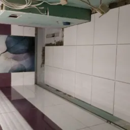 Wnętrze łazienki w trakcie remontu: białe płytki ceramiczne ułożone na ścianie sąsiadują z fragmentem ściany z płyt karton-gips, a na podłodze widoczne płytki w biało-bordowe pasy.