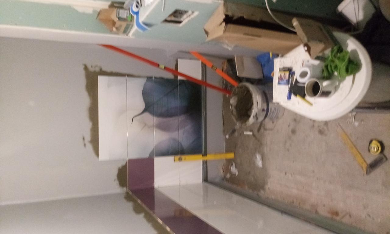 Układanie płytek z motywem liścia na ścianie łazienki, widoczne poziomice, wiadro z zaprawą i narzędzia na podłodze.