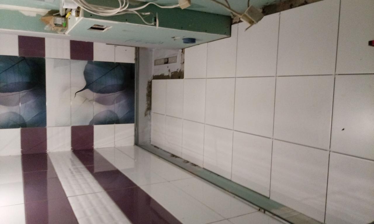 Wnętrze łazienki w trakcie remontu: białe płytki ceramiczne ułożone na ścianie sąsiadują z fragmentem ściany z płyt karton-gips, a na podłodze widoczne płytki w biało-bordowe pasy.