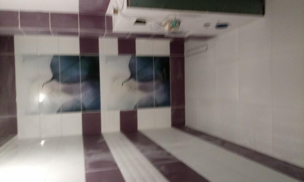 Wykończona łazienka z białymi i bordowymi płytkami ułożonymi w pasy, na ścianie dekoracyjne płytki z motywem roślinnym, widoczny klimatyzator pod sufitem.