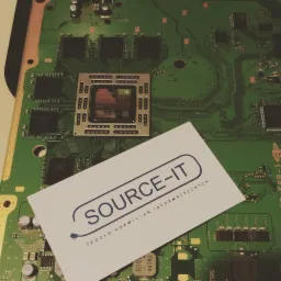 Płyta główna komputera z procesorem i wizytówką firmy SOURCE-IT, specjalizującej się w rozwiązaniach informatycznych.