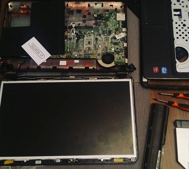 Rozłożony laptop z widoczną płytą główną, ekranem, baterią, dyskiem twardym i narzędziami, etykieta z nazwą firmy na obudowie.