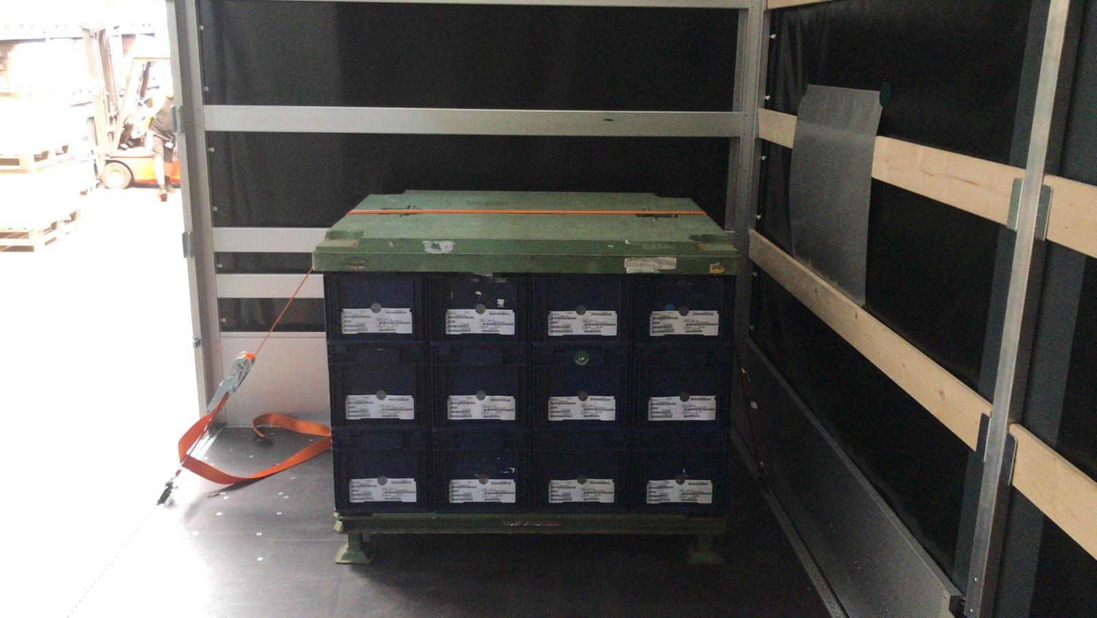 Wnętrze naczepy z zabezpieczonym ładunkiem: skrzynie z etykietami spięte pasem transportowym, w tle wózek widłowy.