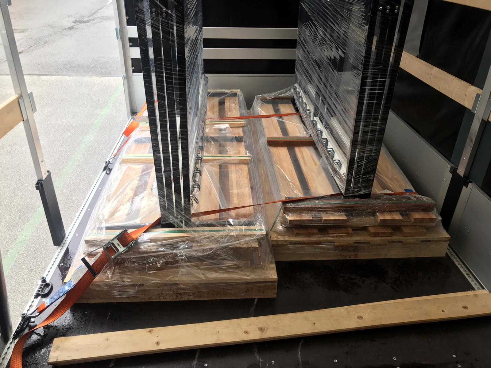 Wnętrze przestrzeni ładunkowej z zabezpieczonymi paletami i metalowymi ramami, owiniętymi folią i spiętymi pomarańczowymi pasami transportowymi.