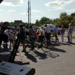 Keyboard i statywy mikrofonowe na zewnątrz, tłum ludzi w tle, prawdopodobnie przygotowania do występu plenerowego.