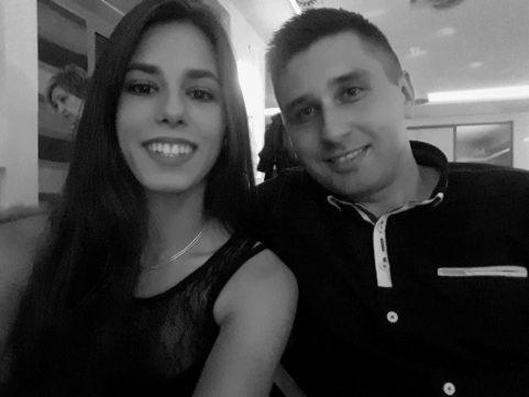 Czarno-białe selfie uśmiechniętej pary: kobieta w koronkowej sukience i mężczyzna w koszuli z białym kołnierzykiem, w tle widoczna część sali.