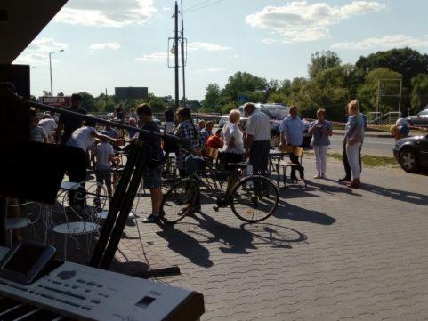 Keyboard i statywy mikrofonowe na zewnątrz, tłum ludzi w tle, prawdopodobnie przygotowania do występu plenerowego.