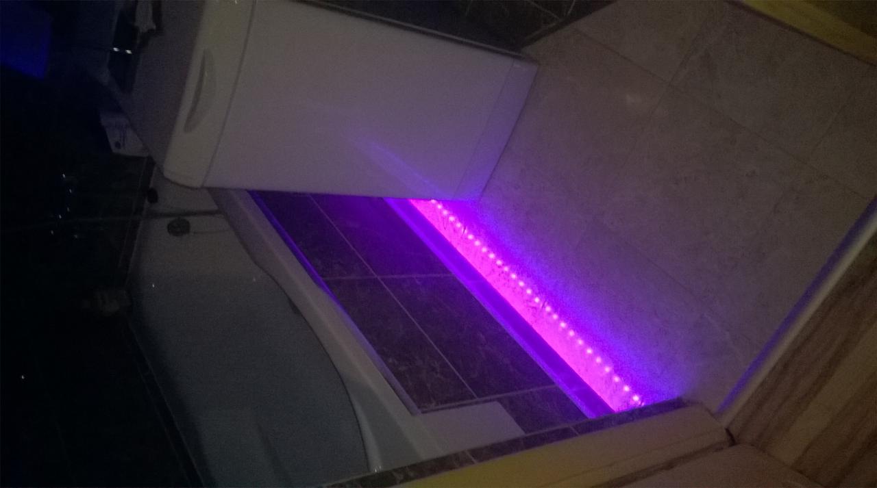 Łazienka z podświetleniem LED w kolorze fioletowym, widoczna wanna, pralka i płytki ceramiczne.