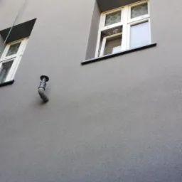 Szara elewacja budynku wielorodzinnego w Lędzinach po malowaniu, widoczne okna z białymi ramami i rura spustowa, lekki gradient koloru na dole ściany.