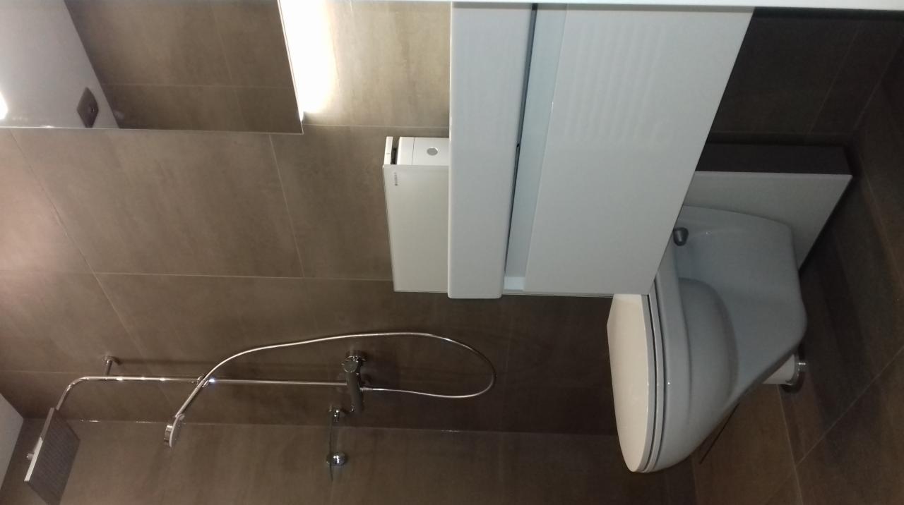 Nowoczesna łazienka z beżowymi płytkami, podwieszaną toaletą z białą zabudową i chromowaną baterią prysznicową