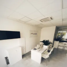 Jasne biuro firmy leasingowej z białymi meblami, komputerami Apple i logotypem na ścianie.