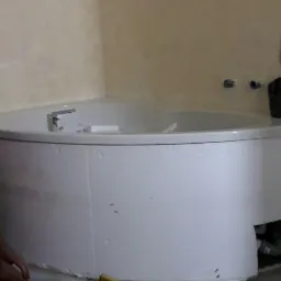 Montaż obudowy wanny narożnej z widocznym poziomem i fragmentami płytek podłogowych w trakcie układania.