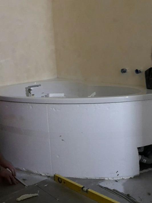 Montaż obudowy wanny narożnej z widocznym poziomem i fragmentami płytek podłogowych w trakcie układania.