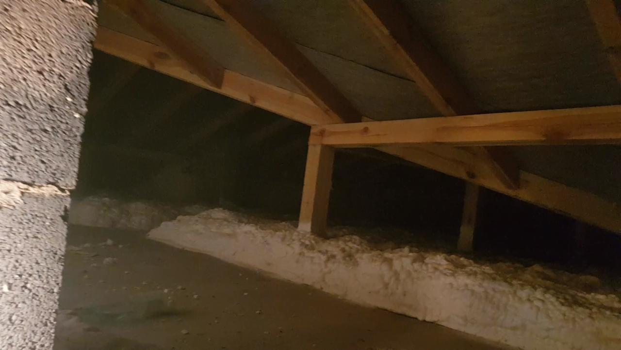 Poddasze ocieplone białą pianką PUR, widoczne drewniane elementy konstrukcji dachu i fragment ściany z szorstką fakturą.