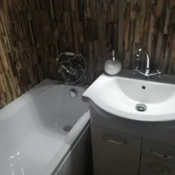 Biała wanna i umywalka z szafką w łazience z dekoracyjną ścianą imitującą drewno.