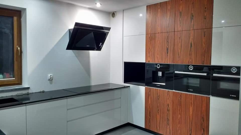 Nowoczesna kuchnia z drewnianymi frontami szafek, czarnym blatem i wbudowanymi urządzeniami AGD marki Bosch.