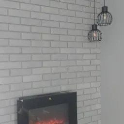Ściana wykończona szarą cegłą dekoracyjną z elektrycznym kominkiem i dwoma wiszącymi lampami w stylu industrialnym.