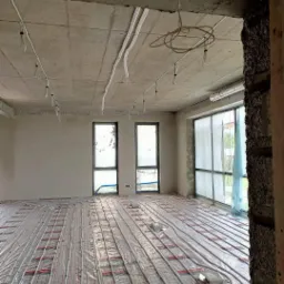 Wnętrze w stanie surowym z instalacją ogrzewania podłogowego i przygotowanymi przewodami elektrycznymi pod sufitem.
