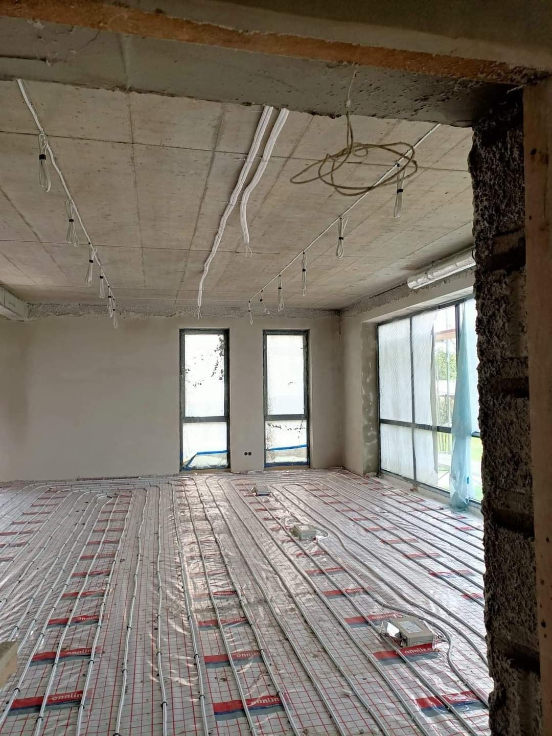 Wnętrze w stanie surowym z instalacją ogrzewania podłogowego i przygotowanymi przewodami elektrycznymi pod sufitem.