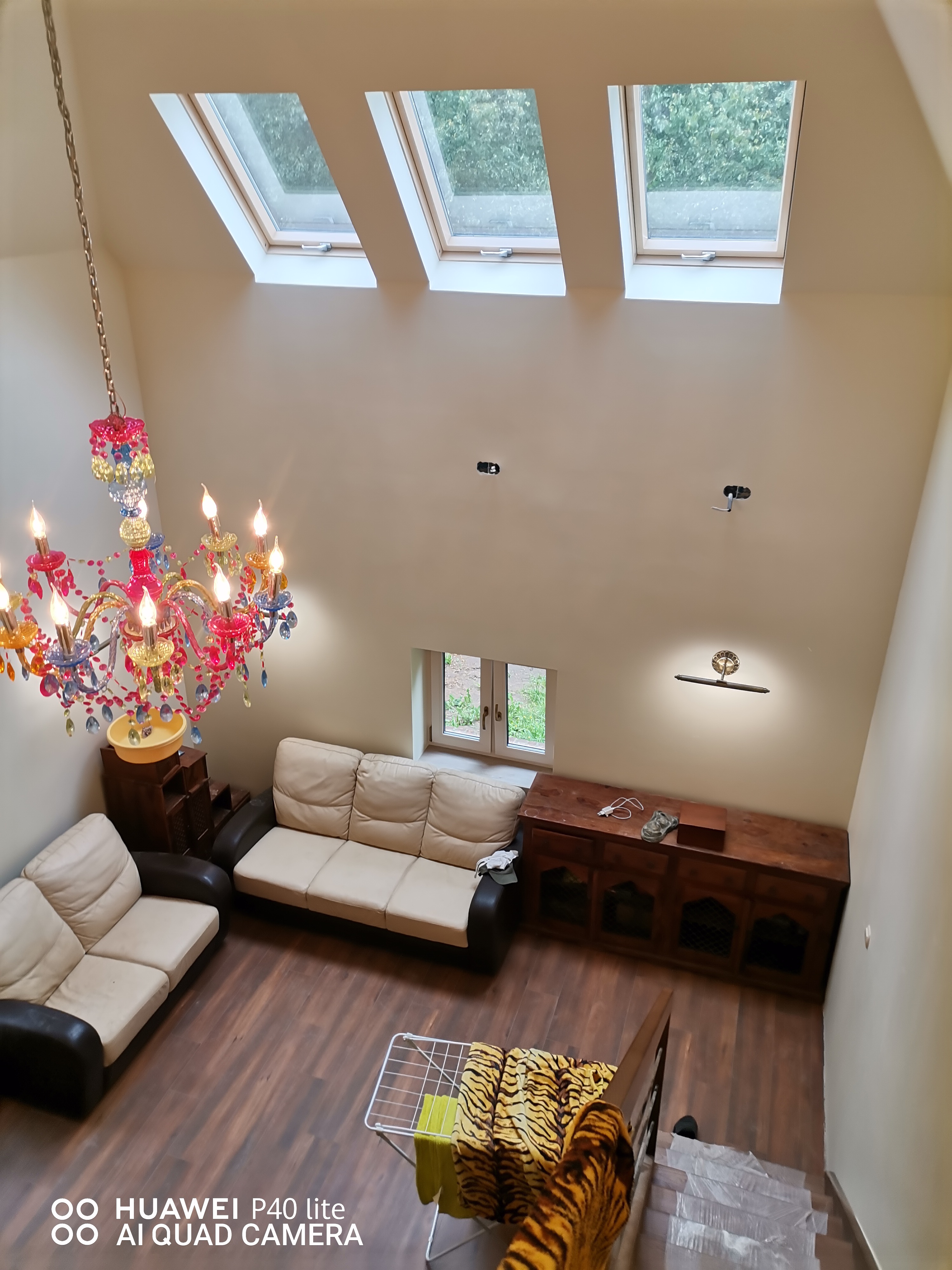 Salon z trzema oknami dachowymi, kolorowym żyrandolem, dwiema sofami i drewnianą podłogą, widok z góry na suszarkę z praniem.