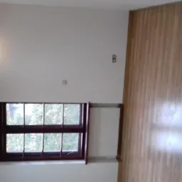 Jasne wnętrze z drewnianą podłogą, oknem z widokiem na zieleń i punktowym oświetleniem na białych ścianach.