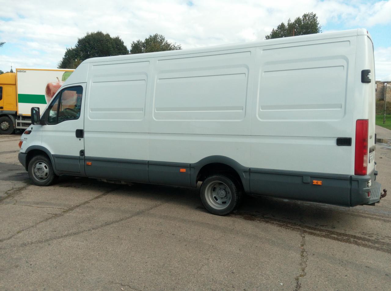 Biały samochód dostawczy Iveco, widok z boku na szarym parkingu, z innym samochodem dostawczym w tle.