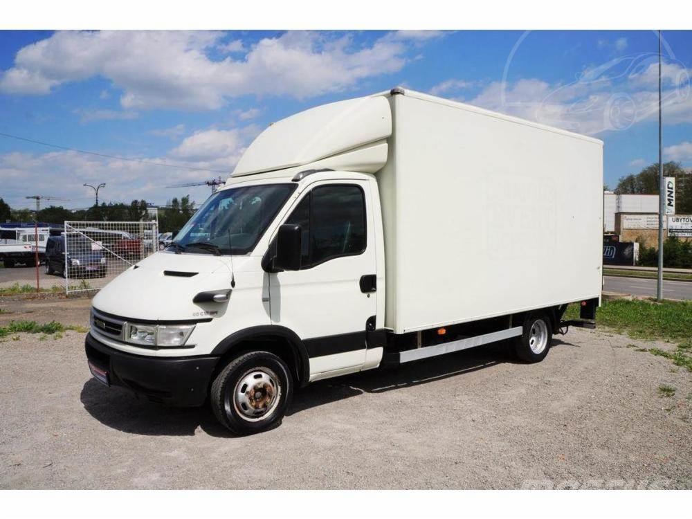 Biały samochód dostawczy z zabudową kontenerową na parkingu, widok z boku, z widocznym lekkim zabrudzeniem na oponach i karoserii, na tle błękitnego nieba z chmurami.