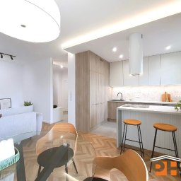 PRESTIGE HOME GROUP Sp. z o.o. - Jasna kuchnia z drewnianymi akcentami, wyspą i hokerami. Parkiet ułożony w jodełkę. W tle salon z szarą sofą i dekoracjami. Całość w nowoczesnym stylu.