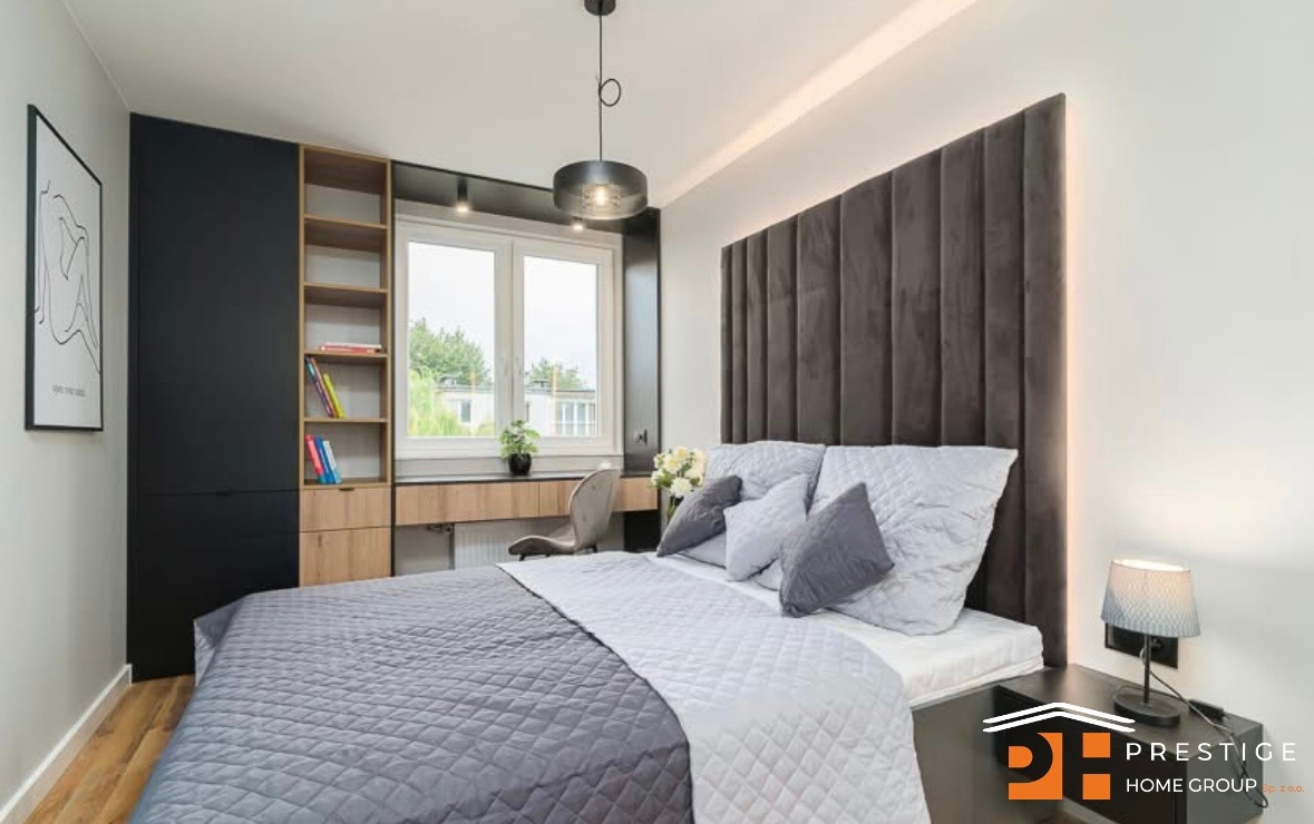 Nowoczesna sypialnia z zabudową meblową: czarna szafa, regał z jasnego drewna, biurko pod oknem i tapicerowany panel za łóżkiem. Minimalistyczny design, oświetlenie punktowe.