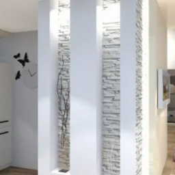 Nowoczesna aranżacja wnętrza z dekoracyjną ścianką działową z kamienia dekoracyjnego, podświetlane wnęki, zegar motyle na szarej ścianie, drewniany stół z filiżanką.