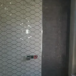 Ściana łazienki w trakcie remontu, z ułożonymi białymi płytkami o falistym wzorze po lewej stronie i ciemnoszarymi płytkami po prawej, widoczne puszki elektryczne w ścianie.