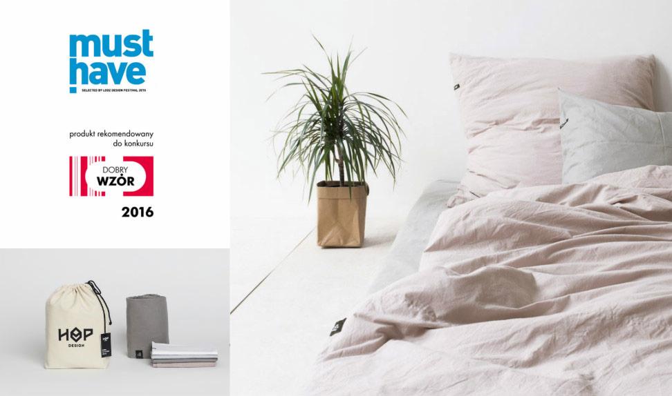 Jasna pościel z lnu w odcieniach beżu i szarości na łóżku, obok roślina w papierowej doniczce, w tle logo 'Must Have' oraz woreczek i ręcznik z logo 'HOP Design'.