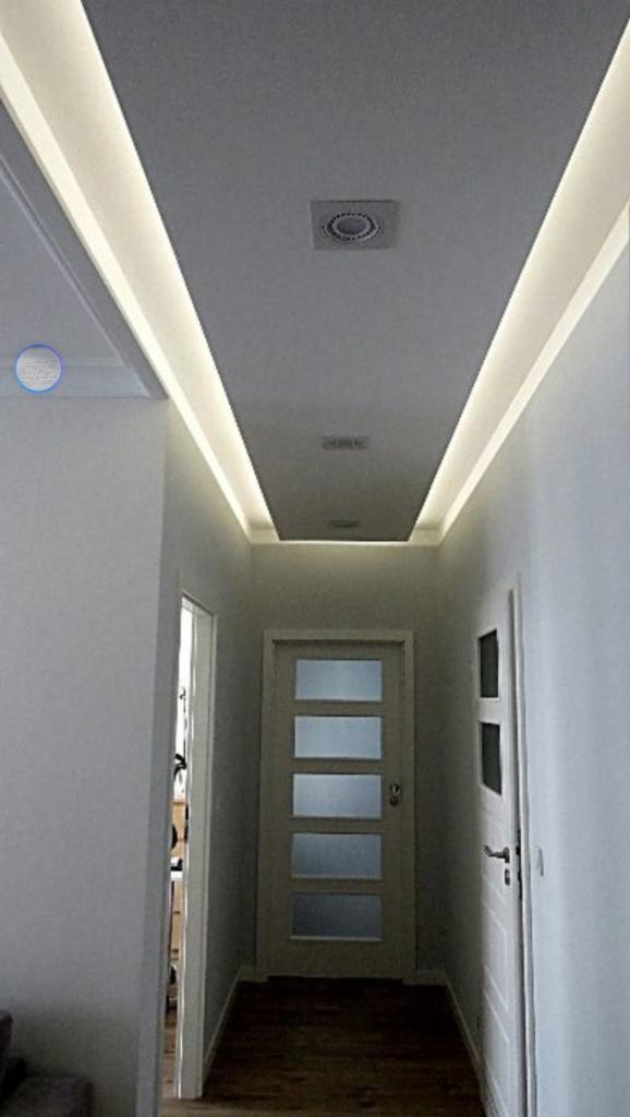 Korytarz w Warszawie z podwieszonym sufitem, oświetleniem LED wzdłuż krawędzi i wentylacją sufitową. Widoczne dwie białe drzwi po bokach.