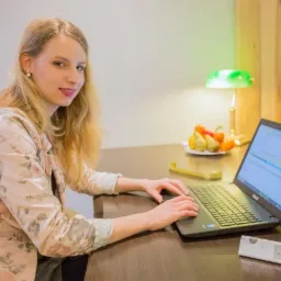 Kobieta z blond włosami pracuje na laptopie przy biurku, na którym leżą owoce, miarka i waga elektroniczna.