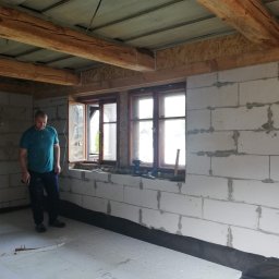Dom-Zbych - Wnętrze w trakcie prac w Somoninie: ściany z betonu komórkowego, drewniane belki stropowe, okno. Widoczny pracownik i narzędzia.