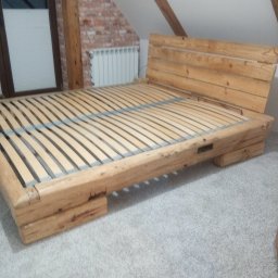 Dom-Zbych - Drewniane łóżko z listwowym stelażem w pokoju na poddaszu. Widoczna ceglana ściana i okno. Naturalne drewno, surowy styl.