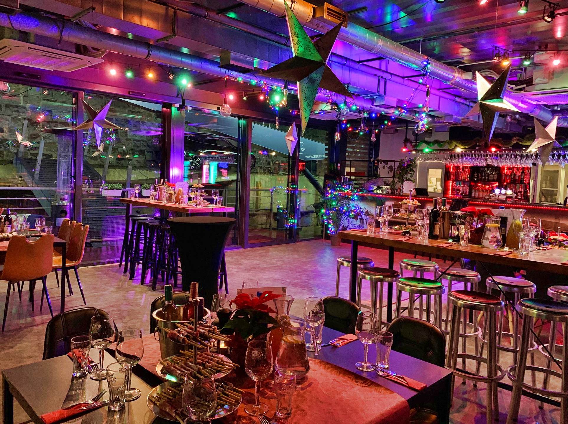 Udekorowana sala eventowa z gwiazdami, kolorowymi lampkami i stołami przygotowanymi do przyjęcia gości, z widocznym barem w tle.