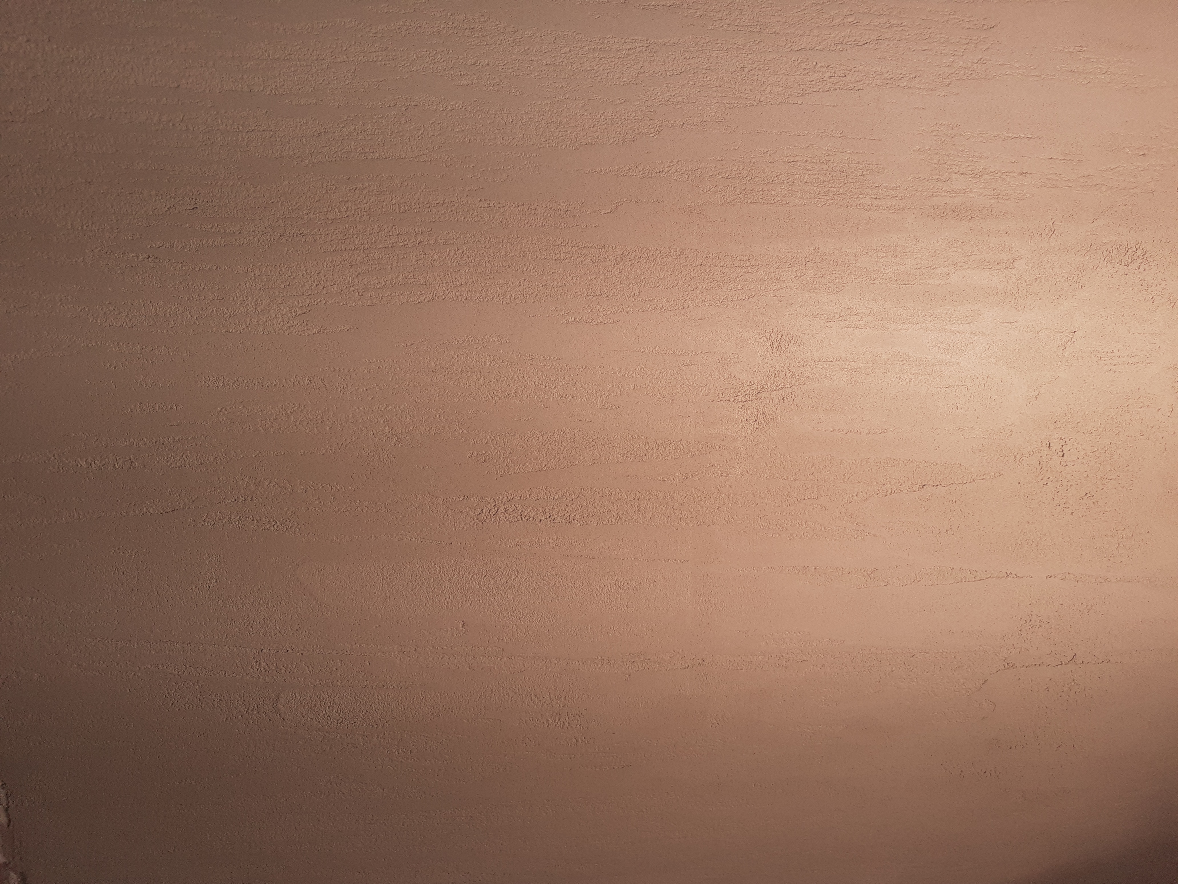 Świeżo nałożona, beżowa gładź szpachlowa na ścianie, widoczne delikatne smugi i nierówności faktury.
