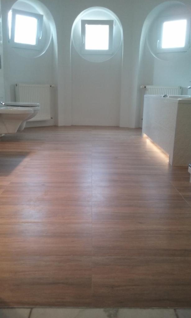 Jasna łazienka z drewnopodobną podłogą z płytek, zaokrąglonymi wnękami okiennymi i podświetleniem pod zabudową umywalki.