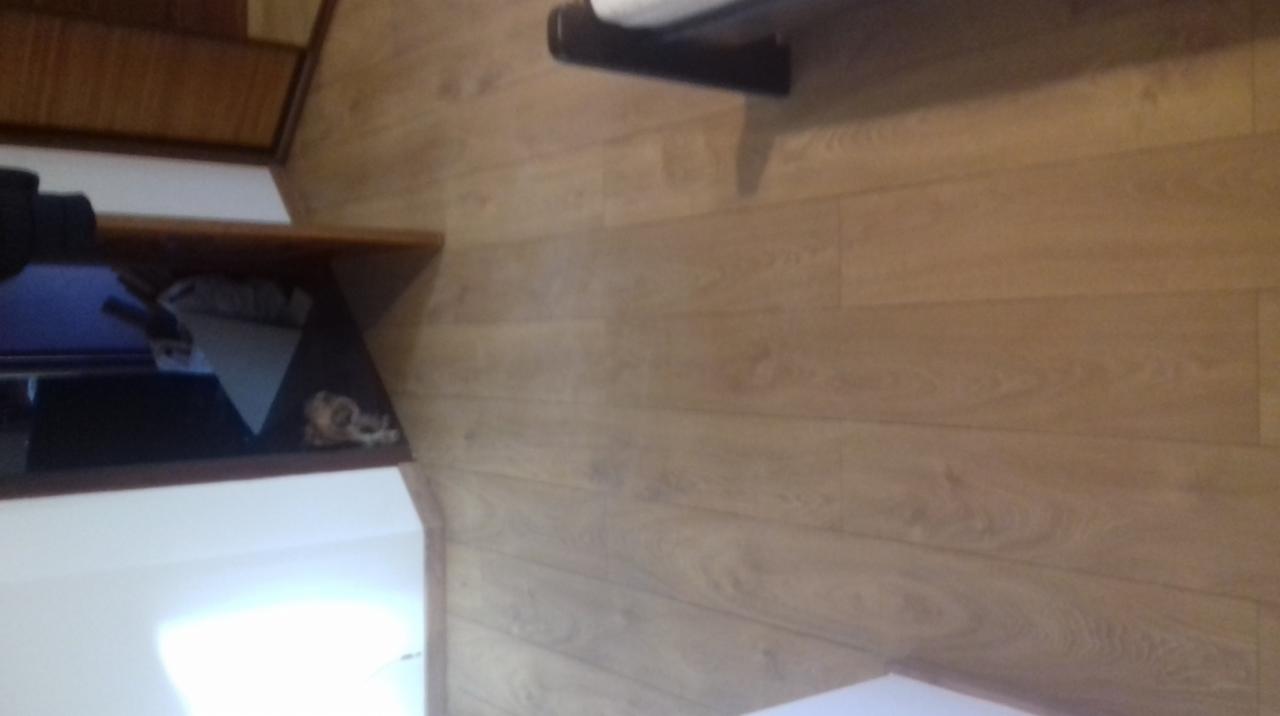 Ułożona podłoga z paneli laminowanych w odcieniach jasnego drewna, widoczna z bliska, z fragmentem mebli w tle.