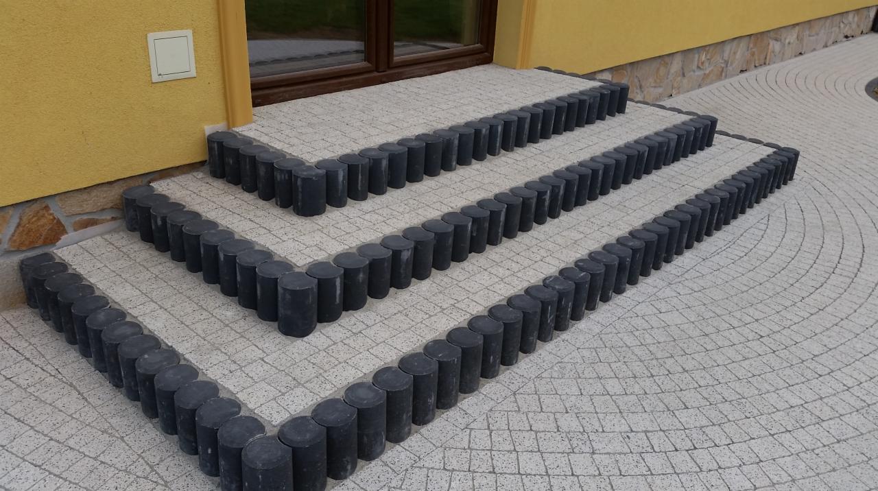 Schody wejściowe do domu wyłożone jasnoszarą kostką brukową z obrzeżem z ciemnych, okrągłych elementów.
