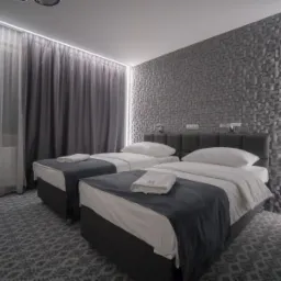 Pokój hotelowy z dwoma łóżkami pojedynczymi, szarą narzutą i dekoracyjną ścianą z efektem 3D, oświetlenie LED.