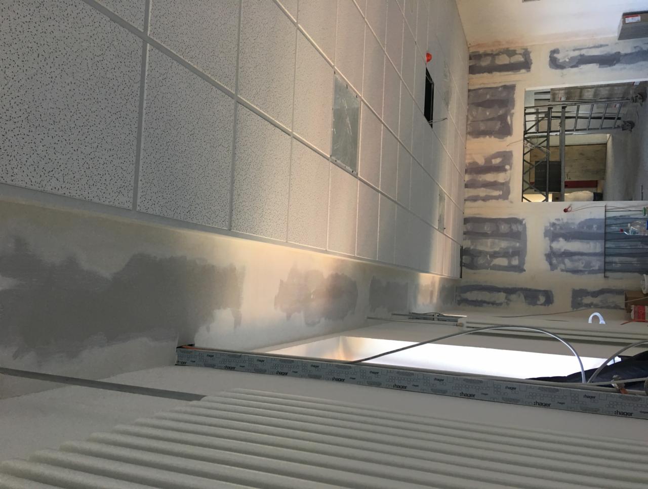 Montaż sufitu kasetonowego w pomieszczeniu w trakcie prac wykończeniowych; widoczne ślady szpachlowania na ścianach, metalowa konstrukcja w tle.