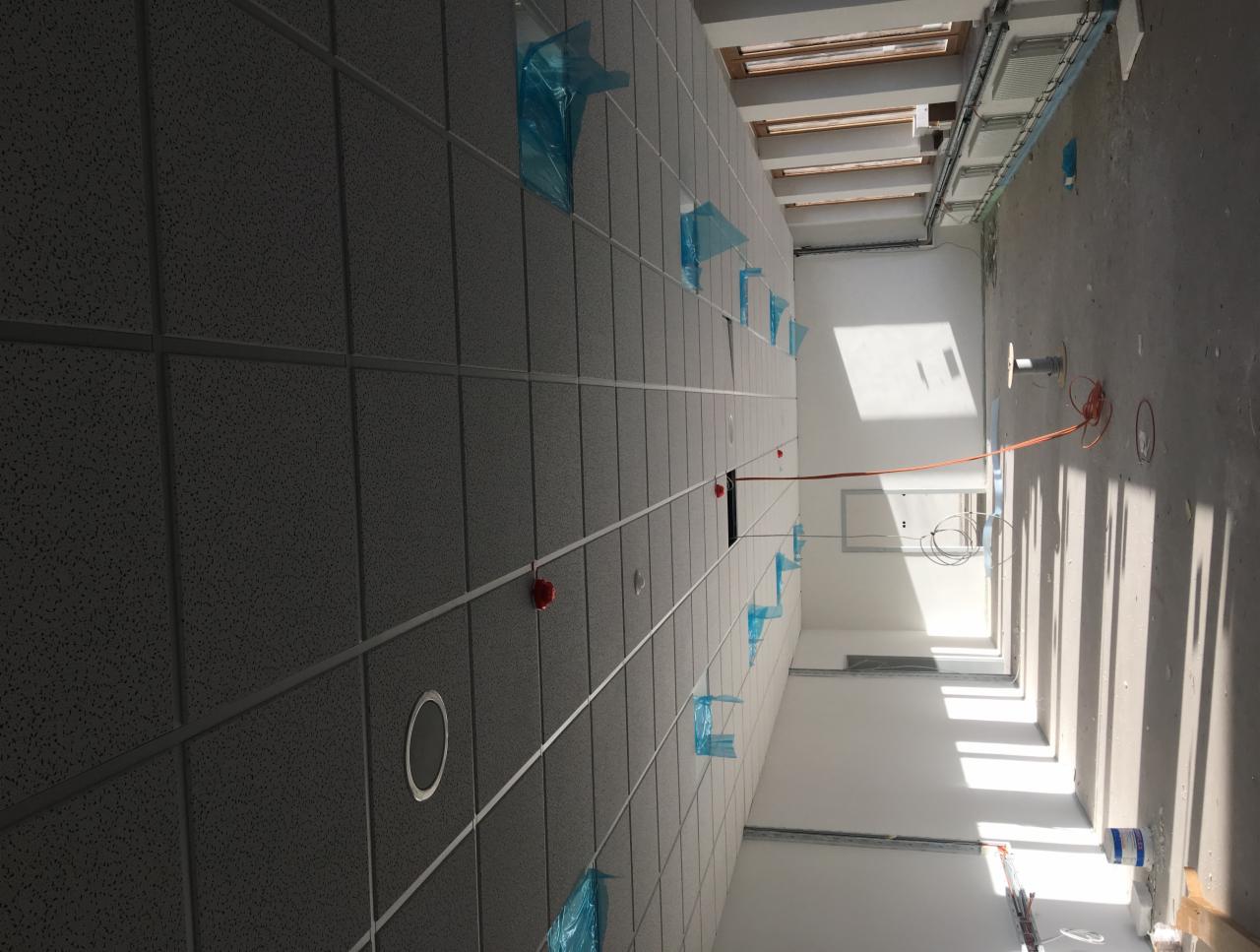 Montaż sufitu podwieszanego kasetonowego w jasnym pomieszczeniu, zabezpieczone elementy instalacji niebieską folią, widoczne przewody elektryczne i puszki instalacyjne.