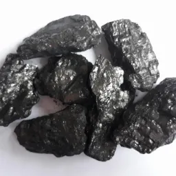 Kawałki antracytu, błyszczące i czarne, ułożone na białym tle, z widoczną strukturą węgla.