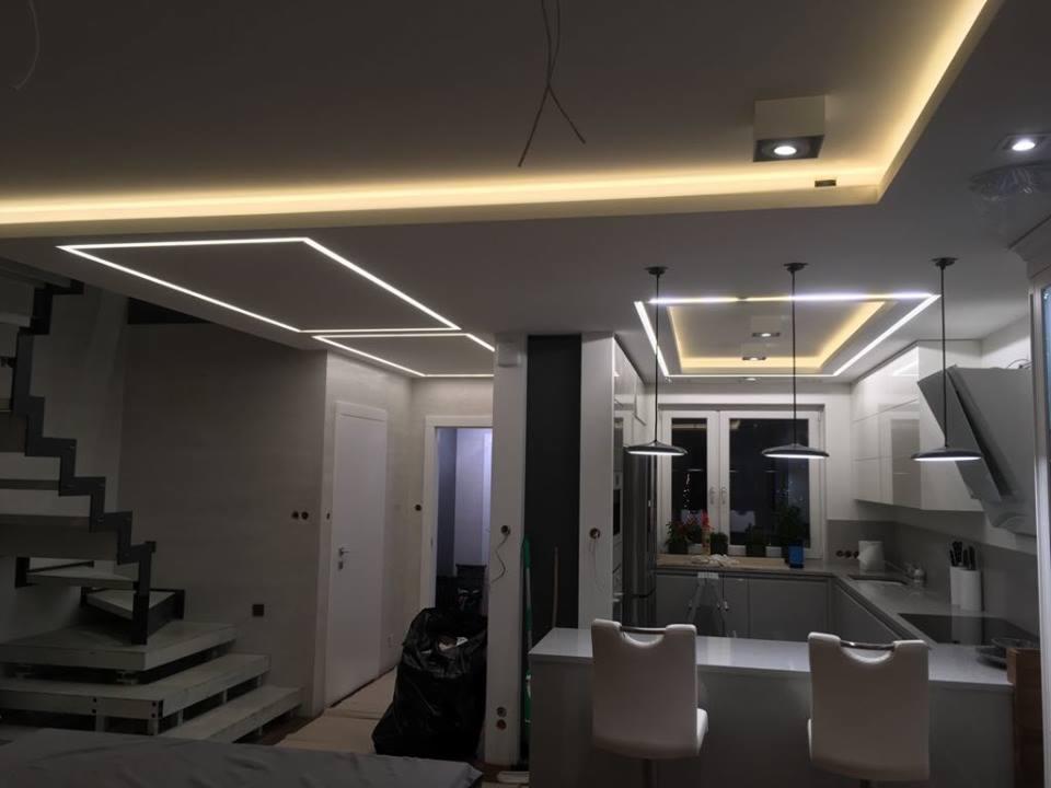 Nowoczesne oświetlenie sufitowe LED w salonie z aneksem kuchennym, widoczne geometryczne kształty i minimalistyczne lampy wiszące.