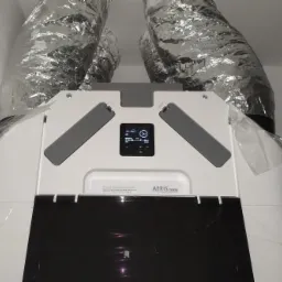 Centrala wentylacyjna z rekuperacją AERIS, widoczne srebrne rury wentylacyjne i panel sterowania z wyświetlaczem.