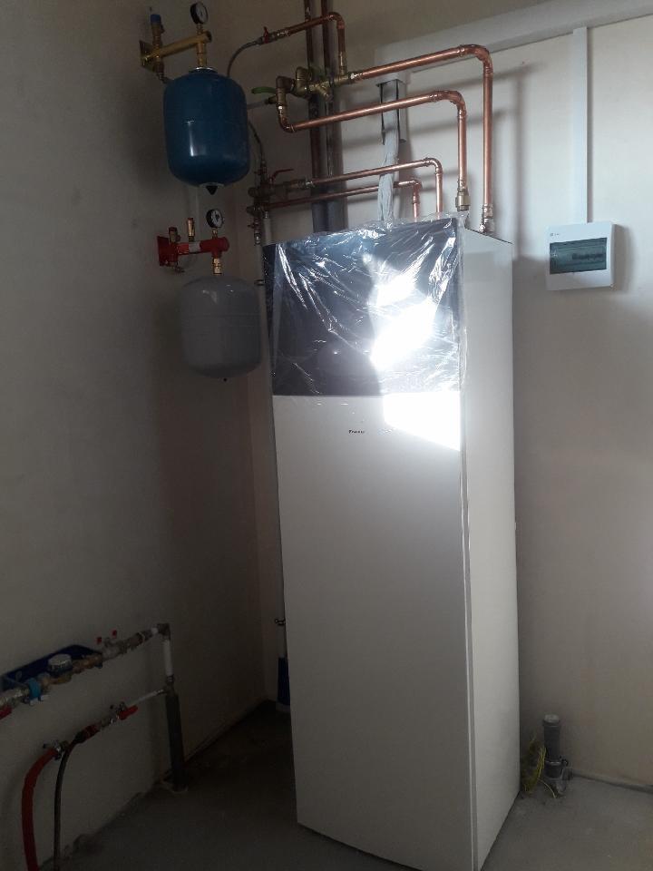 Nowa, biała pompa ciepła Daikin, jeszcze w folii ochronnej, z widocznymi instalacjami hydraulicznymi z miedzianych rur i dwoma zbiornikami ciśnieniowymi w pomieszczeniu technicznym.