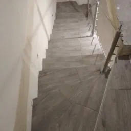 Schody wyłożone płytkami imitującymi drewno, z metalową balustradą, widok z góry.