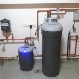 Kompletny system uzdatniania wody w kotłowni wykończonej drewnem, z dwoma zbiornikami, filtrem, pompą i miedzianą instalacją.